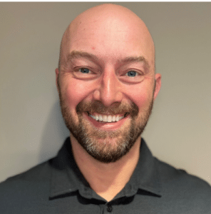 Smiling male dental professional in dark shirt against neutral background at Northwest Family Dental Care