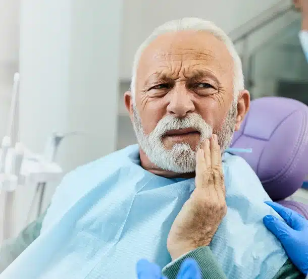 Elderly man in dental bib experiencing tooth pain in dental office setting.
