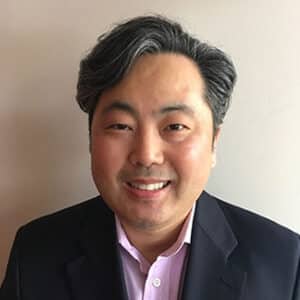 Professional headshot of an Asian man in business attire smiling at camera against neutral background.