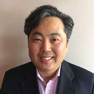 Professional headshot of an Asian man in business attire smiling at camera against neutral background.